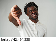 Young African Man Giving Thumbs Down Gesture Against a Neutral Background. Стоковое фото, фотограф Сергей Толмачёв / Фотобанк Лори