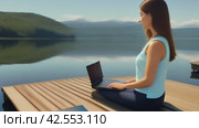 Woman in sportswear sits on a wooden dock near the lake and uses a laptop. Стоковое AI-видео, аниматор Юрий Поздников / Фотобанк Лори