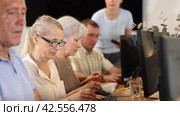 Interested senior woman in glasses attending computer class, learning basics of digital technology under guidance of teacher standing in blurred background. Стоковое видео, видеограф Яков Филимонов / Фотобанк Лори