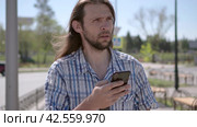 Front view of a walking man with a beard, suddenly bewildered by the news while checking the contents of his smart phone. Стоковое видео, видеограф EStarodubov / Фотобанк Лори