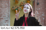 Знак рукой победа. Portrait of happy mime young woman in a black coat with victory hand sign and looking smiling at the camera. Стоковое видео, видеограф EStarodubov / Фотобанк Лори