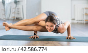 Young attractive smiling woman practicing side crow pose variation parsva bacasana yoga on mat in yoga studio. Стоковое фото, фотограф Яков Филимонов / Фотобанк Лори