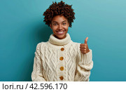 ctp afroamerican young woman in white sweater with thumbs up while pointing to right. Стоковое AI-изображение, AI-художник Юлия Гапеенко / Фотобанк Лори