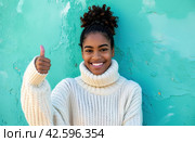 ctp afroamerican young woman in white sweater with thumbs up while pointing to right. Стоковое AI-изображение, AI-художник Юлия Гапеенко / Фотобанк Лори