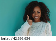 ctp afroamerican young woman in white sweater with thumbs up while pointing to right. Стоковое AI-изображение, AI-художник Юлия Гапеенко / Фотобанк Лори