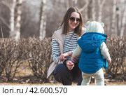 A handsome, cheerful little boy of two years old walks with his mother on the street in the spring. The kid is playing against the background of spring flowers in the park. The concept of parenthood, childhood and family. Стоковое фото, фотограф Photojuli / Фотобанк Лори