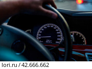 Close up of Twilight Drive With Focus on Speedometer and Steering Wheel. Close-up of cars speedometer, drivers hand on steering wheel during an evening drive. Car transport concept. Copy ad text space. Стоковое фото, фотограф Aleksandr Golubev / Фотобанк Лори