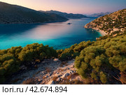Sunset in laguna of azure Aegean Sea with lush mountains, fluffy clouds, yacht, summer weather. Nature landscape in East Turkey. Concept of vacation, recreation and travel. Стоковое AI-изображение, AI-художник Aleksandr Golubev / Фотобанк Лори