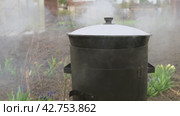 Food is cooked in a cauldron outdoors in the yard. Steam from boiling water. Стоковое видео, видеограф Дмитрий Кобзев / Фотобанк Лори