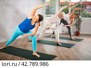 Women of different ages stretching in Extended Side Angle Pose or Utthita Parsvakonasana during yoga class in gym studio. Стоковое фото, фотограф Яков Филимонов / Фотобанк Лори