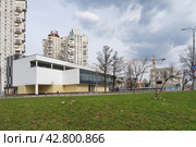 Склон с зеленой молодой весенней травой на фоне построенного торгово-развлекательного комплекса в Зеленограде. На фоне жилые многоэтажные дома, стоящийся объект с подъёмным краном, небо с облаками. Новостройка 2024 года. Редакционное фото, фотограф Сергей Никифоров-Гордеев / Фотобанк Лори