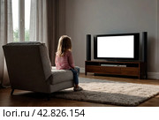 Rear view of little girl kid 5-6 year old watching tv sits on armchair looking cartoon. Adorable dependency girl child, empty isolated screen. Television addiction tv concept. Copy ad text space. Стоковое AI-изображение, AI-художник Aleksandr Golubev / Фотобанк Лори