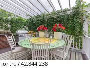 A beautiful terrace with a gazebo covered with ivy. White garden furniture and red flowers on the table. Стоковое фото, фотограф Алексей Климкин / Фотобанк Лори