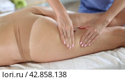 Closeup of hands of professional masseuse performing anti-cellulite thigh and bum massage to young female client in spa center. Стоковое видео, видеограф Яков Филимонов / Фотобанк Лори