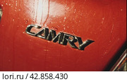 Крупный план блестящего шильдика Camry. На багажнике красного автомобиля надпись Camry. Блестит на солнце. Плавное наложение камеры. Краснодар, Россия, 1 декабря 2023 года. Редакционное видео, видеограф Воловодов Владимир / Фотобанк Лори