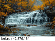 Picturesque waterfall in the forest in autumn. The water rushes forcefully over multi-level rocky rapids, creating a striking contrast with the warm colors of the autumn foliage surrounding the pond. The leaves of the trees, painted in golden and copper tones, glow against the background of dark blue water and stones, which adds peace and harmony to the scene. Стоковое AI-изображение, AI-художник Анна Кривицкая / Фотобанк Лори