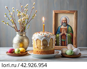 Orthodox Easter. Easter cake, painted eggs, icons, faces of saints, flowers, church candles and Easter decor on a wooden table in an old village house. Стоковое AI-изображение, AI-художник Photojuli / Фотобанк Лори