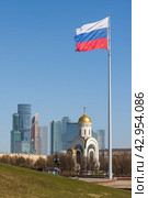 Вид на флагшток с флагом России, церковь и небоскрёбы. Красивая церковь на фоне высотных зданий. Сочетание традиций и целеустремлённости в будущее в современной России. Церковь Георгия Победоносца и международный деловой центр, город Москва, Россия. (2023 год). Редакционное фото, фотограф Андрей Степанов / Фотобанк Лори