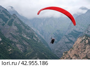 red paraglider flies against the background of mountains and clouds, rear view. Стоковое фото, фотограф Александр Довянский / Фотобанк Лори
