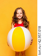 Happy little girl wearing red swimsuit holding beachball on yellow background. Summer vacation and childhood concept. Active lifestyle. Стоковое фото, фотограф Ирина Михайличенко / Фотобанк Лори