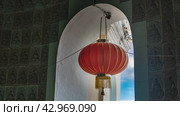 A bright red Chinese lantern is suspended in the window opening against the background of the blue sky. Ornaments on the interior tiled walls. Malaysia. Penang. Kek Lok Si Temple. Close-up (2023 год). Стоковое фото, фотограф Вера Ивановна Кубарева / Фотобанк Лори