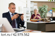 Adult employee playing games on smartphone at workplace in office. Стоковое фото, фотограф Яков Филимонов / Фотобанк Лори