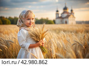 Russian Russian girl in a white dress and a Russian headscarf holds golden ears of wheat against the background of a ripening field and an Orthodox church. The concept of planting and harvesting a rich harvest. Rural landscape. Стоковое AI-изображение, AI-художник Photojuli / Фотобанк Лори