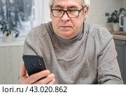 Hoary old man looking at web camera, holding phone, talking with children, wife online. Senior grandpa smiling chatting with friends, family via video call. Modern technologies and older generation. Стоковое фото, фотограф Марина Демидюк / Фотобанк Лори