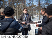 Уличный музыкант и певец выступает на открытом воздухе в парке. Молодой человек играет на гитаре и поет песни. Юноши в черных куртках слушают музыку. Город Магадан, Магаданская область, Россия. (2018 год). Редакционное фото, фотограф Андрей Степанов / Фотобанк Лори