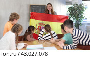 Group of curious preteen learners and young female teacher with flag of Spain in classroom of academy. Стоковое видео, видеограф Яков Филимонов / Фотобанк Лори