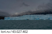 A wall of cracked blue ice stretches over a glacial lake. Thawed ice floes, icebergs float in turquoise water. Coastal mountains in clouds and fog. Perito Moreno glacier. Lago Argentino. El Calafate. Стоковое фото, фотограф Вера Ивановна Кубарева / Фотобанк Лори