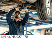 A young car mechanic repairs the suspension of a passenger car. The concept of a car service. Стоковое AI-изображение, AI-художник Ярославский Максим / Фотобанк Лори