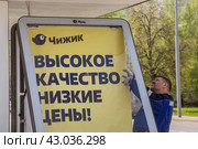 Рабочий монтирует рекламу магазина "Чижик" на остановке общественного транспорта в городе Москве, Россия (2024 год). Редакционное фото, фотограф Николай Винокуров / Фотобанк Лори