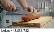 Man cuts thin slices of sausage on a wooden board with a knife. Close-up of the hands. Стоковое видео, видеограф EStarodubov / Фотобанк Лори