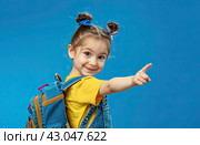 A little girl with a large school backpack on a blue background points her finger at an empty space. Copy space. Стоковое AI-изображение, AI-художник Ярославский Максим / Фотобанк Лори