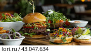 A large burger with a meat patty and filling on the table with spices and ingredients. Стоковое AI-изображение, AI-художник Ярославский Максим / Фотобанк Лори