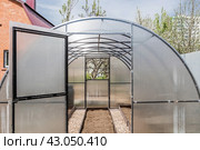 A new greenhouse made of polyethylene and polycarbonate with new beds made of Wood-polymer composite. Preparing for the spring garden season. Installation of a greenhouse in a suburban area. Стоковое фото, фотограф Photojuli / Фотобанк Лори