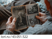 Elderly person holding old family photographs in hands. Стоковое AI-изображение, AI-художник Антон Гвоздиков / Фотобанк Лори