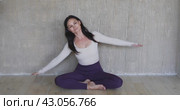 A woman leading a healthy lifestyle performs lateral bends in Badha Konasana, trains while sitting in a room in sports overalls near the wall. Стоковое видео, видеограф Сергей Чайко / Фотобанк Лори