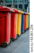 Row of colorful waste containment cylinders on asphalt sidewalk. Стоковое AI-изображение, AI-художник Юрий Поздников / Фотобанк Лори