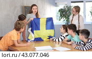 Group of curious preteen learners and young female teacher with flag of Sweden in classroom of academy. Стоковое видео, видеограф Яков Филимонов / Фотобанк Лори
