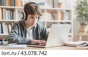 Focused young student engaged in online learning, wearing headphones and studying on a laptop in a home setting surrounded by books. Стоковое AI-видео, аниматор Lena Bereberdina / Фотобанк Лори