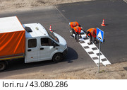 Summer road works. A team of road workers in orange vests apply warning white markings to a speed bump or sleeping policeman on an asphalt road. Seasonal work on city roads. View from above. Стоковое фото, фотограф Виктория Катьянова / Фотобанк Лори