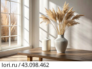 A modern white ceramic vase with dried grass on a wooden table. Scandinavian interior. An empty white wall with a shadow from the window. Стоковое AI-изображение, AI-художник Photojuli / Фотобанк Лори