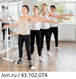 Dancing positive women and men engaged in group class perform exercise near ballet barre, standing in 2nd position of ballet stance in dance studio. Стоковое фото, фотограф Яков Филимонов / Фотобанк Лори