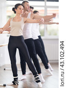 Dancing positive women and men engaged in group class perform exercise near ballet barre, standing in 2nd position of ballet stance in dance studio. Стоковое фото, фотограф Яков Филимонов / Фотобанк Лори