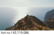 A woman stands boldly on a cliff with a breathtaking ocean view in the background. The clear sky and expansive sea highlight the scene vast openness. Стоковое видео, видеограф Igor Tichonow / Фотобанк Лори