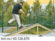 Moscow, Russia - July 2, 2021:Push scooter stunt on the urban sport ground in summer day. Boy shows  trick. Jumping. Healthy lifestyle. Extreme sports is popular among youth. Back view. Редакционное фото, фотограф YuryKara / Фотобанк Лори
