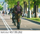 Moscow, Russia - May 15, 2023: One man drive motor scooter in public Gorky park in spring day. Other cycling next. Using of the sharing motor scooters service. Front view. Редакционное фото, фотограф YuryKara / Фотобанк Лори