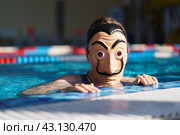 Moscow region, Russia - March 17, 2023: Somebody put on Salvador Dali mask in the swimming pool. Blue water background. Bright sun. Abstraction. Close up conceptual image. Looking at camera. Редакционное фото, фотограф YuryKara / Фотобанк Лори
